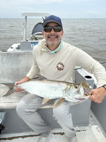 Smiling angler on a boat holding a silver tarpon